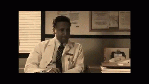 Man In Lab Coat And Tie At Desk In Front Of Bulletin Board GIF