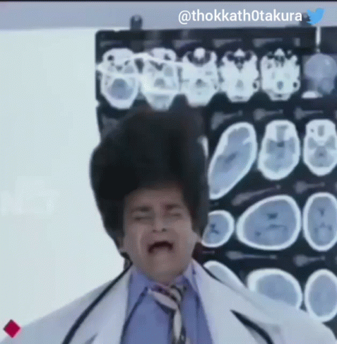 A Man In A Lab Coat And Tie Stands In Front Of An X-Ray Of A Brain GIF