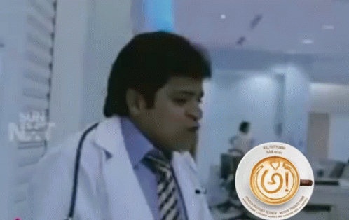 A Man In A Lab Coat Is Sitting In Front Of A Cup Of Coffee That Says Nespresso GIF