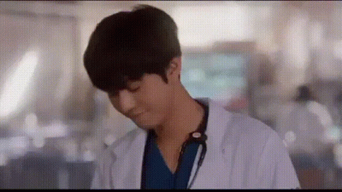 A Man In A Lab Coat With A Stethoscope Around His Neck Is Standing In A Hallway . GIF