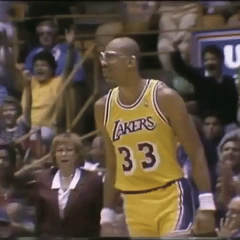 A Man In A Lakers Jersey Is Standing In Front Of A Crowd Of People . GIF