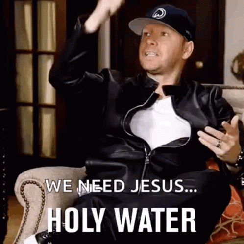 A Man In A Leather Jacket And Hat Is Sitting On A Couch And Saying We Need Jesus ... Holy Water . GIF