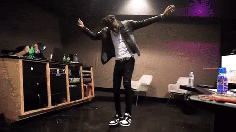 A Man In A Leather Jacket Is Dancing In A Room With A Table And Chairs GIF