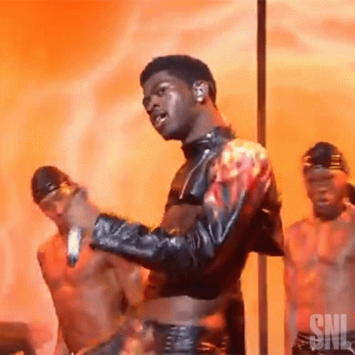 A Man In A Leather Jacket Is Dancing On A Pole With Two Men Behind Him . GIF