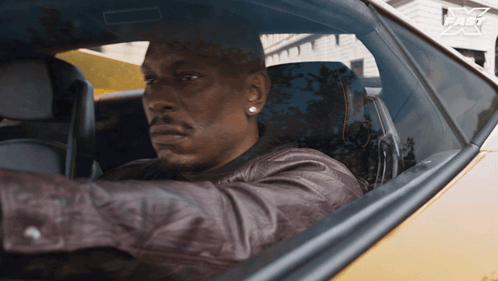 A Man In A Leather Jacket Is Driving A Car With A Fast Logo On The Side GIF