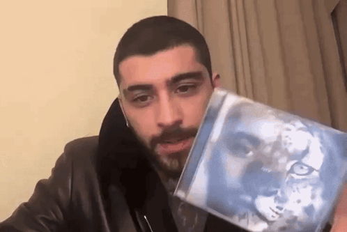 A Man In A Leather Jacket Is Holding A Cd With A Picture Of A Lion On It . GIF