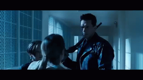 A Man In A Leather Jacket Is Holding A Gun Next To A Girl . GIF