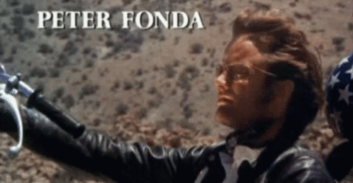 A Man In A Leather Jacket Is Holding A Motorcycle Handlebars And The Name Peter Fonda Is Visible Above Him GIF