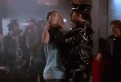A Man In A Leather Jacket Is Holding Another Man 'S Head In A Crowd Of People . GIF