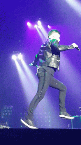 A Man In A Leather Jacket Is Jumping In The Air With A Microphone GIF