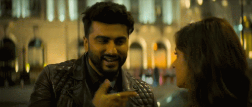 A Man In A Leather Jacket Is Pointing At A Woman 'S Face GIF