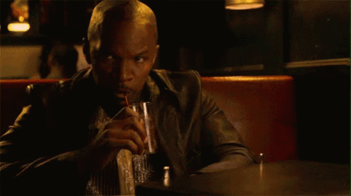 A Man In A Leather Jacket Is Sitting At A Table Drinking A Drink . GIF