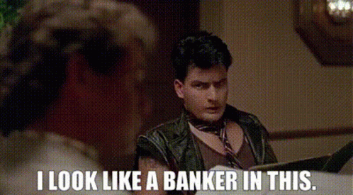 A Man In A Leather Jacket Is Sitting At A Table Reading A Book And Says `` I Look Like A Banker In This '' GIF