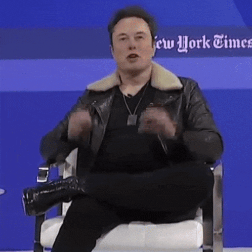 a man in a leather jacket is sitting in a chair in front of a blue wall that says new york times