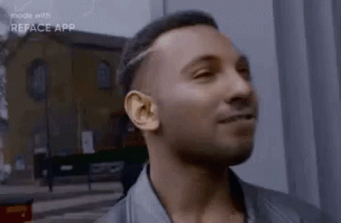 a man in a leather jacket is smiling and looking at the camera while standing in front of a building .