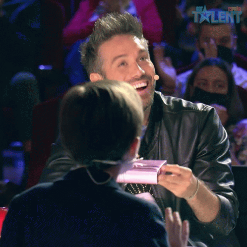 A Man In A Leather Jacket Is Smiling In Front Of A Sign That Says ' Estrella Talent ' GIF