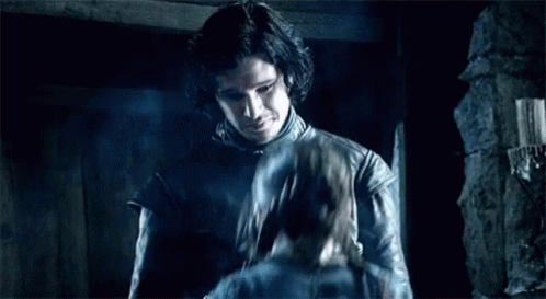 A Man In A Leather Jacket Is Standing In A Dark Room Holding A Sword . GIF