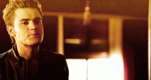 A Man In A Leather Jacket Is Standing In A Dark Room Looking At The Camera . GIF