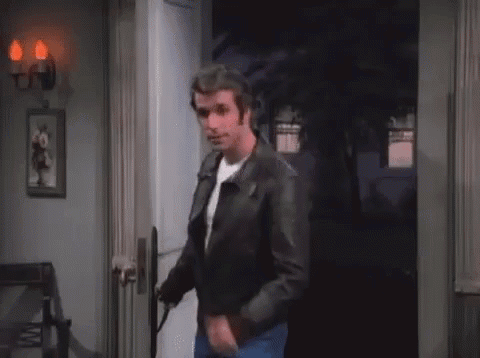 A Man In A Leather Jacket Is Standing In A Doorway Holding A Gun . GIF