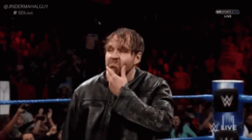 A Man In A Leather Jacket Is Standing In A Wrestling Ring With His Hand To His Chin . GIF
