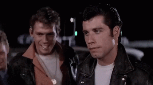 A Man In A Leather Jacket Is Standing In Front Of A Group Of Men In A Parking Lot . GIF