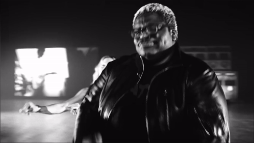 A Man In A Leather Jacket Is Standing In Front Of A Large M GIF