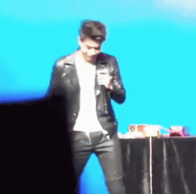 a man in a leather jacket is standing in front of a microphone