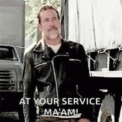 A Man In A Leather Jacket Is Standing In Front Of A Truck With The Words `` At Your Service , Ma 'Am '' . GIF