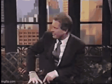 A Man In A Leather Jacket Is Standing In Front Of A Window In A Living Room . GIF