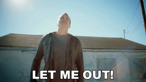 A Man In A Leather Jacket Stands In Front Of A Building With The Words Let Me Out GIF