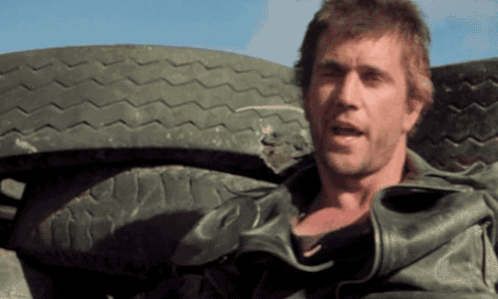 A Man In A Leather Jacket Stands In Front Of A Large Tire GIF