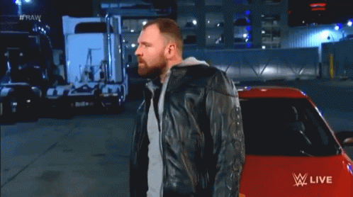 A Man In A Leather Jacket Stands In Front Of A Red Car With Fire Coming Out Of It And The Words Raw On The Bottom GIF