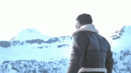 A Man In A Leather Jacket Stands In Front Of A Snowy Landscape GIF