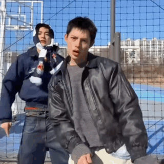 A Man In A Leather Jacket Stands Next To Another Man In A Scarf GIF