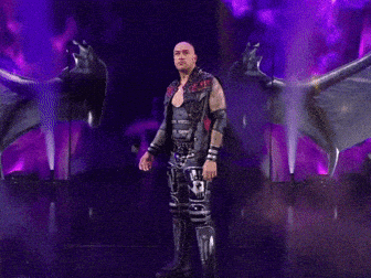 A Man In A Leather Vest With The Letter R On It Stands On A Stage GIF
