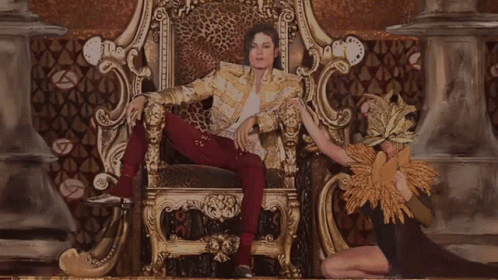 A Man In A Leopard Print Jacket Is Sitting On A Gold Throne GIF