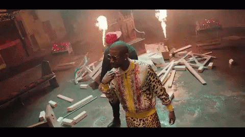 a man in a leopard print jacket is standing in a room with a lot of wood and fire .