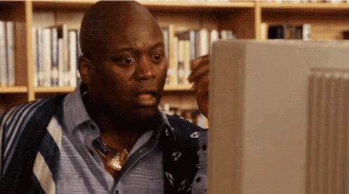A Man In A Library Looking At A Computer Monitor GIF