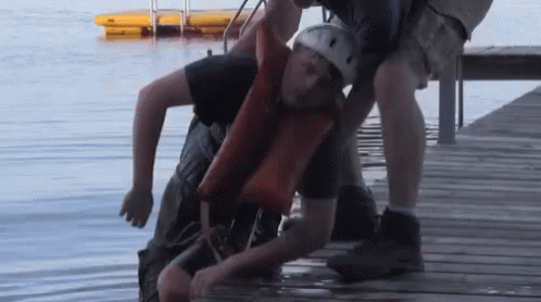 A Man In A Life Jacket Is Being Lifted Out Of The Water GIF