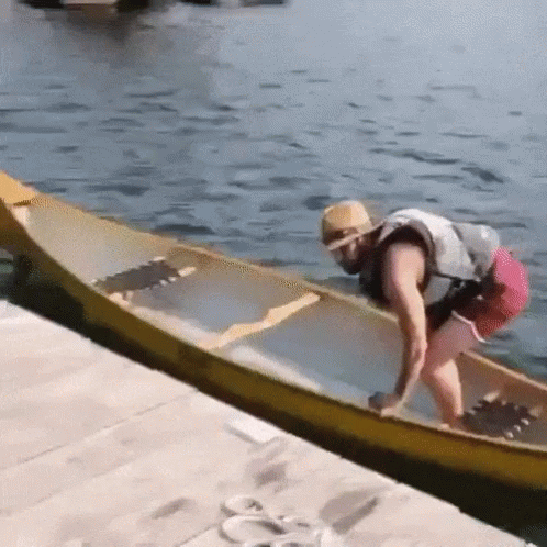 A Man In A Life Jacket Is Pushing A Yellow Canoe Into The Water . GIF