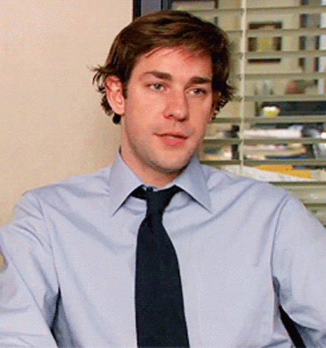 A Man In A Light Blue Shirt And Black Tie Looks At The Camera GIF