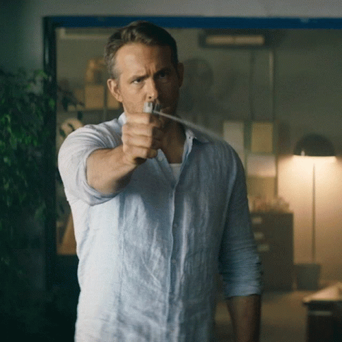 A Man In A Light Blue Shirt Is Pointing A Gun GIF