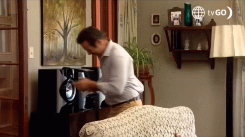 A Man In A Living Room With A Tvgo Logo On The Wall GIF