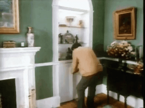 A Man In A Living Room With Green Walls And A Fireplace GIF