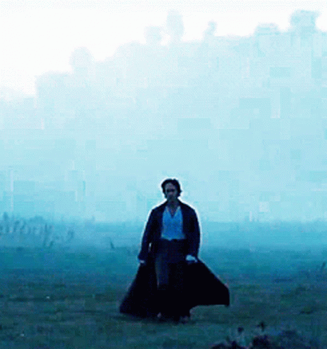 A Man In A Long Black Coat Is Walking Through A Field GIF
