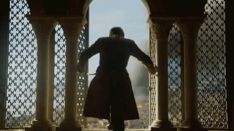 A Man In A Long Coat Is Standing In Front Of A Window With Columns . GIF