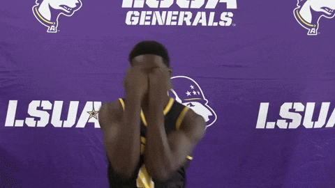 a man in a lsua jersey smiles in front of a purple backdrop