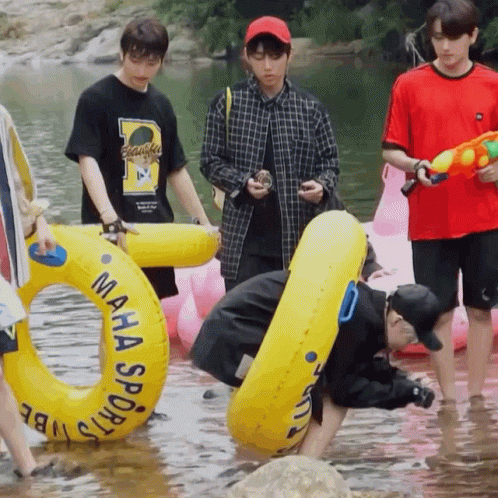 A Man In A Maha Sports Shirt Is Kneeling In The Water Holding A Water Gun GIF