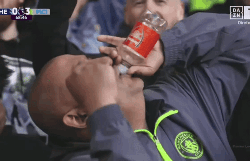 A Man In A Manchester City Jacket Drinks From A Bottle GIF