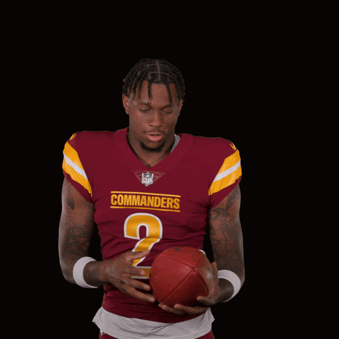 A Man In A Maroon Commanders Jersey Holds A Football GIF